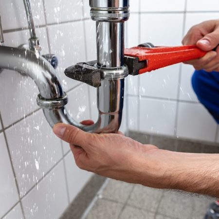 Plumber Repairing Sink Pipe Leakage Male Plumber's Hand Repairing Sink Pipe Leakage With Adjustable Wrench
