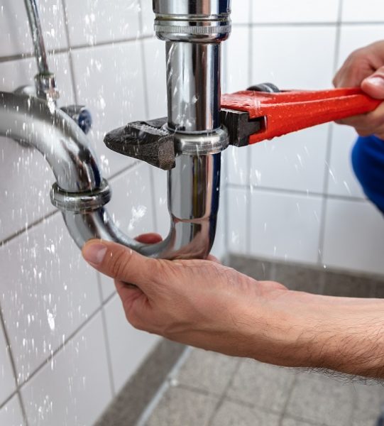 Plumber Repairing Sink Pipe Leakage Male Plumber's Hand Repairing Sink Pipe Leakage With Adjustable Wrench